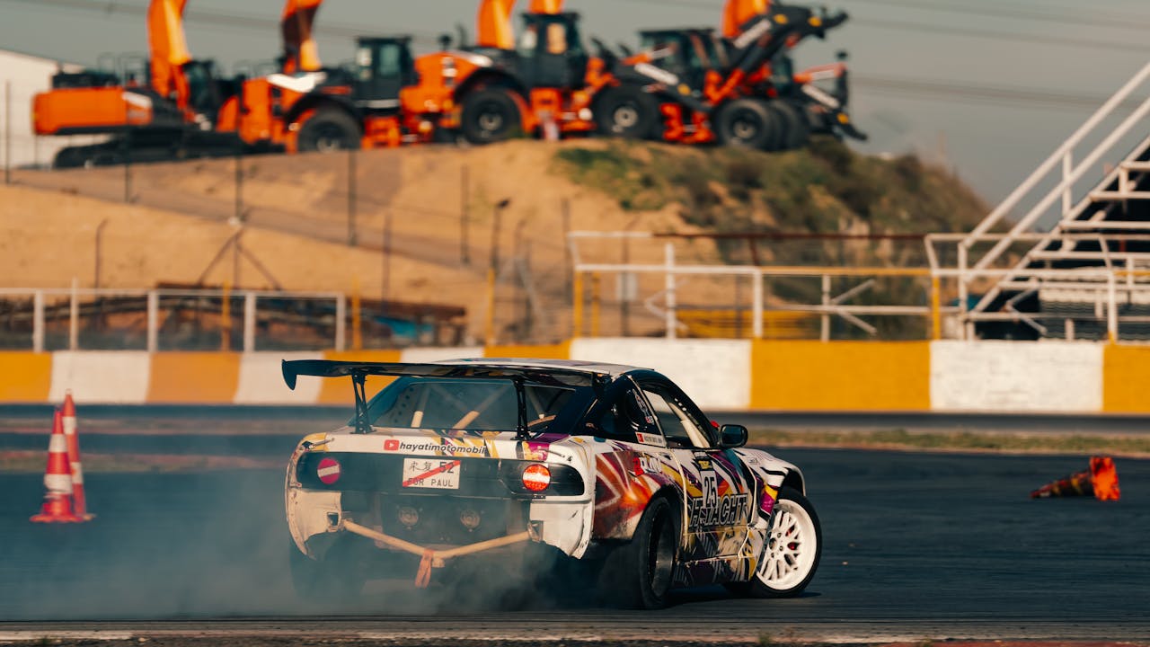 A vibrant race car performs a drift on a track with construction equipment in the background.