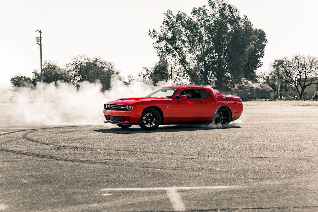 A vibrant red muscle car performing a drift, creating smoke on an open asphalt area in Sacramento, CA.
